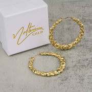 Pair of 10k gold heart-twisted round hoop earrings displayed beside a Nolters Gold box.