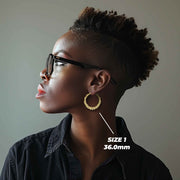 Side profile of a woman wearing 36mm 10k gold heart-themed twisted round hoop earrings.