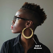 Side profile of a woman wearing 80mm 10k gold heart-themed twisted round hoop earrings.