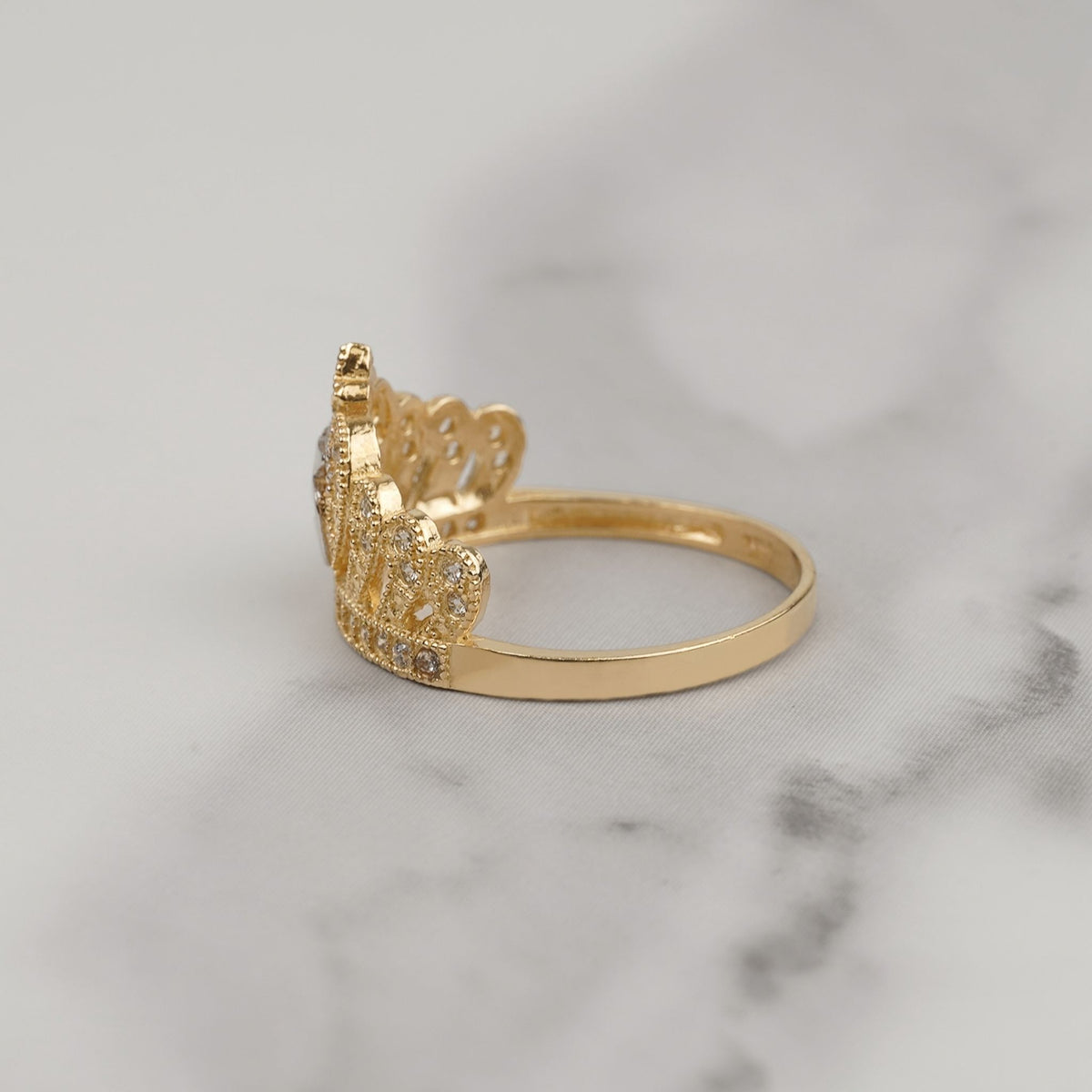Side view of two-tone gold quinceañera crown ring with cubic zirconia detailing on marble.