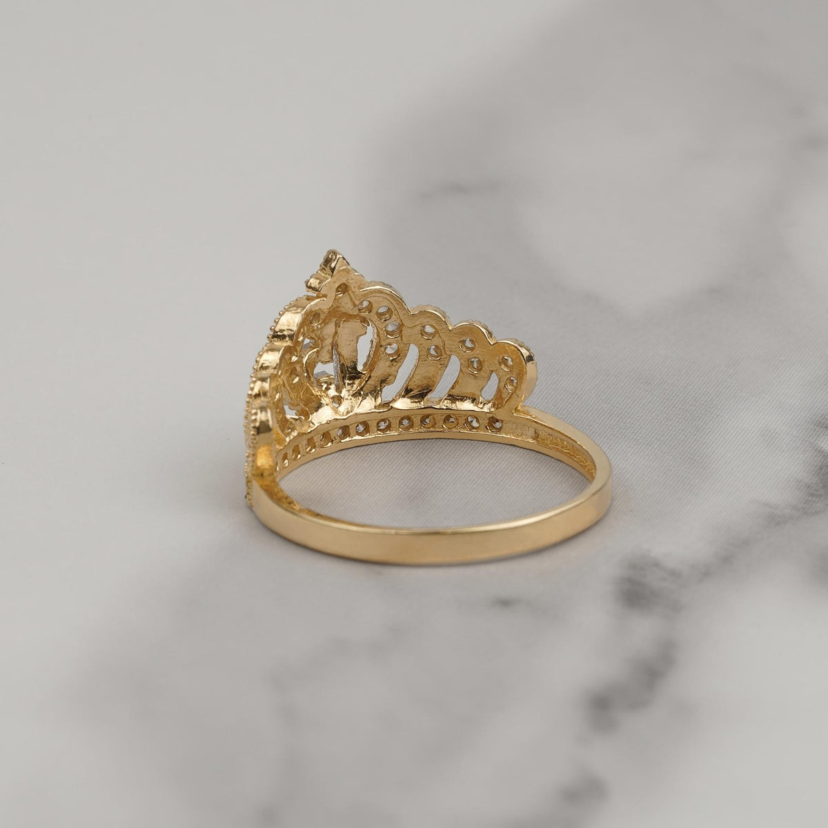 Back view of two-tone gold quinceañera crown ring with filigree band on marble.