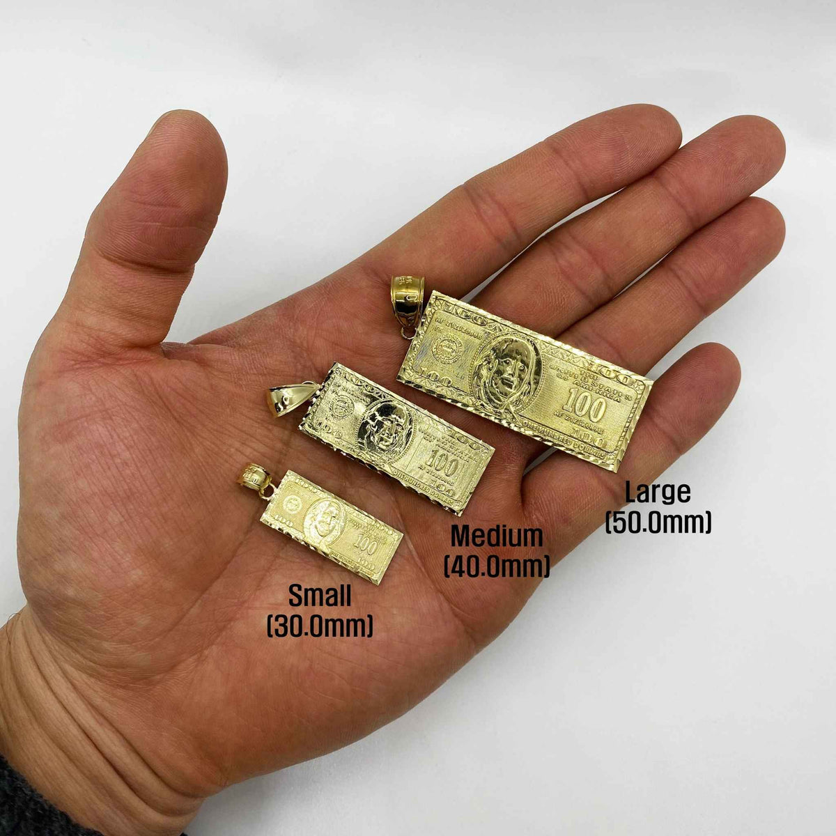 Small, Medium, and Large gold hundred dollar bill pendants displayed on an open hand for scale.