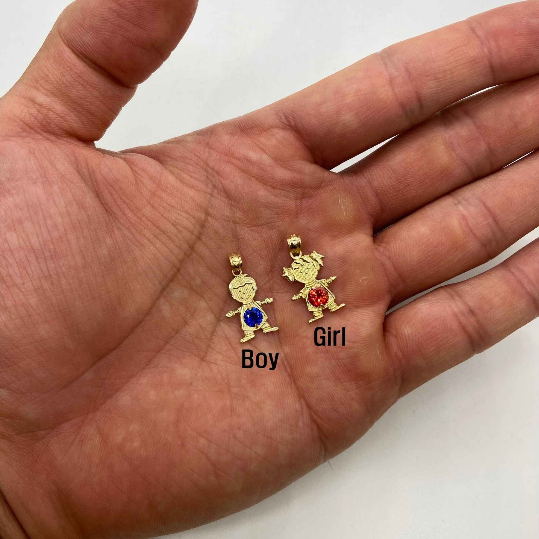Open hand holding labeled gold boy and girl pendants with red and blue gemstones.