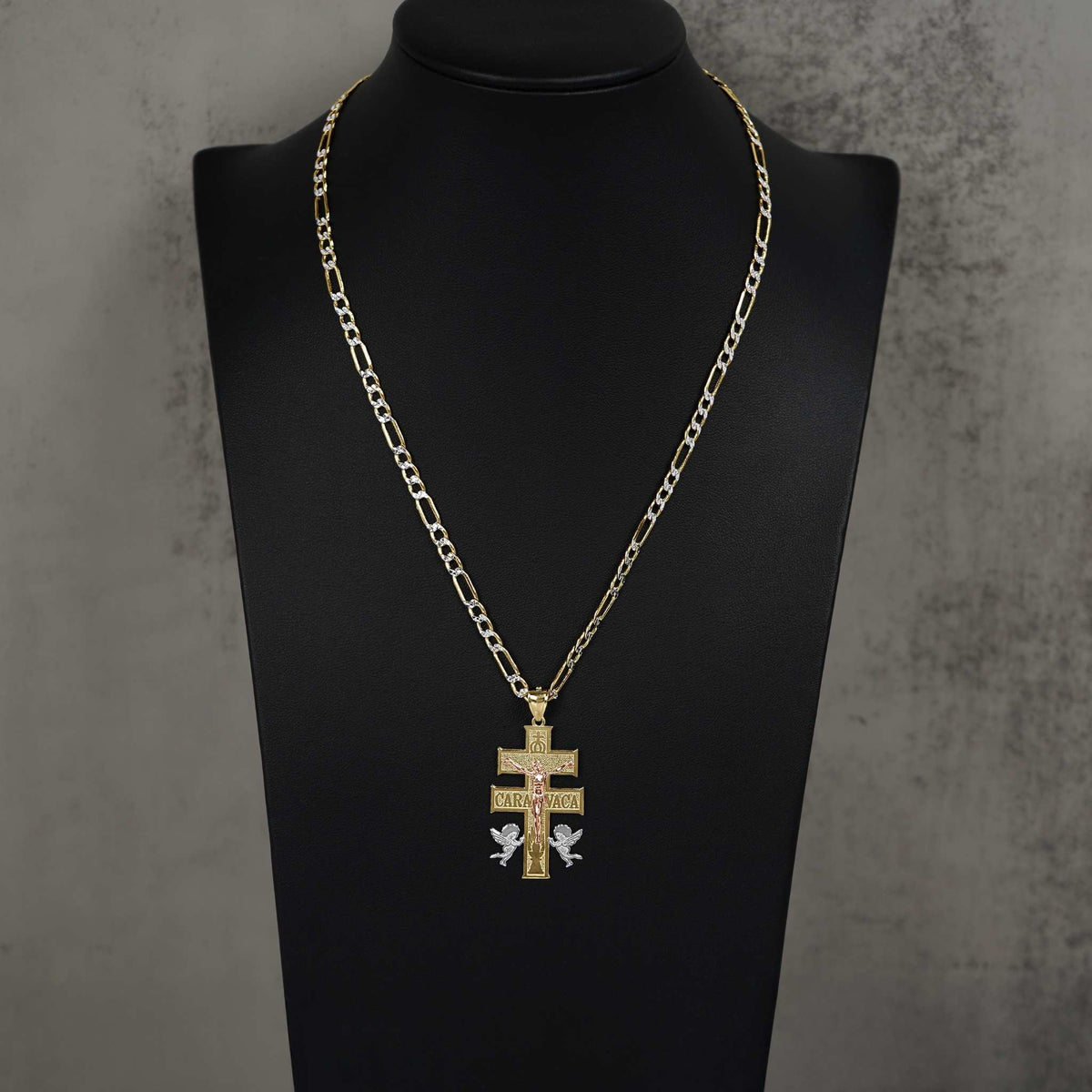 Gold Caravaca cross pendant on a Figaro chain, displayed on a black jewelry bust.