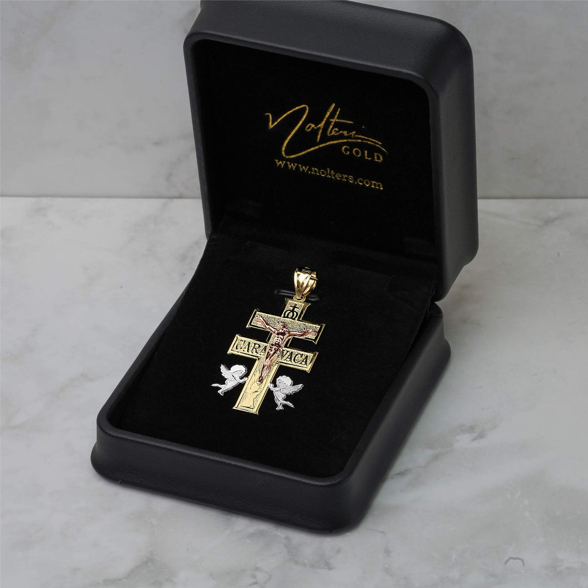 Gold Caravaca crucifix pendant displayed inside an open black velvet Nocturne Gold jewelry box.