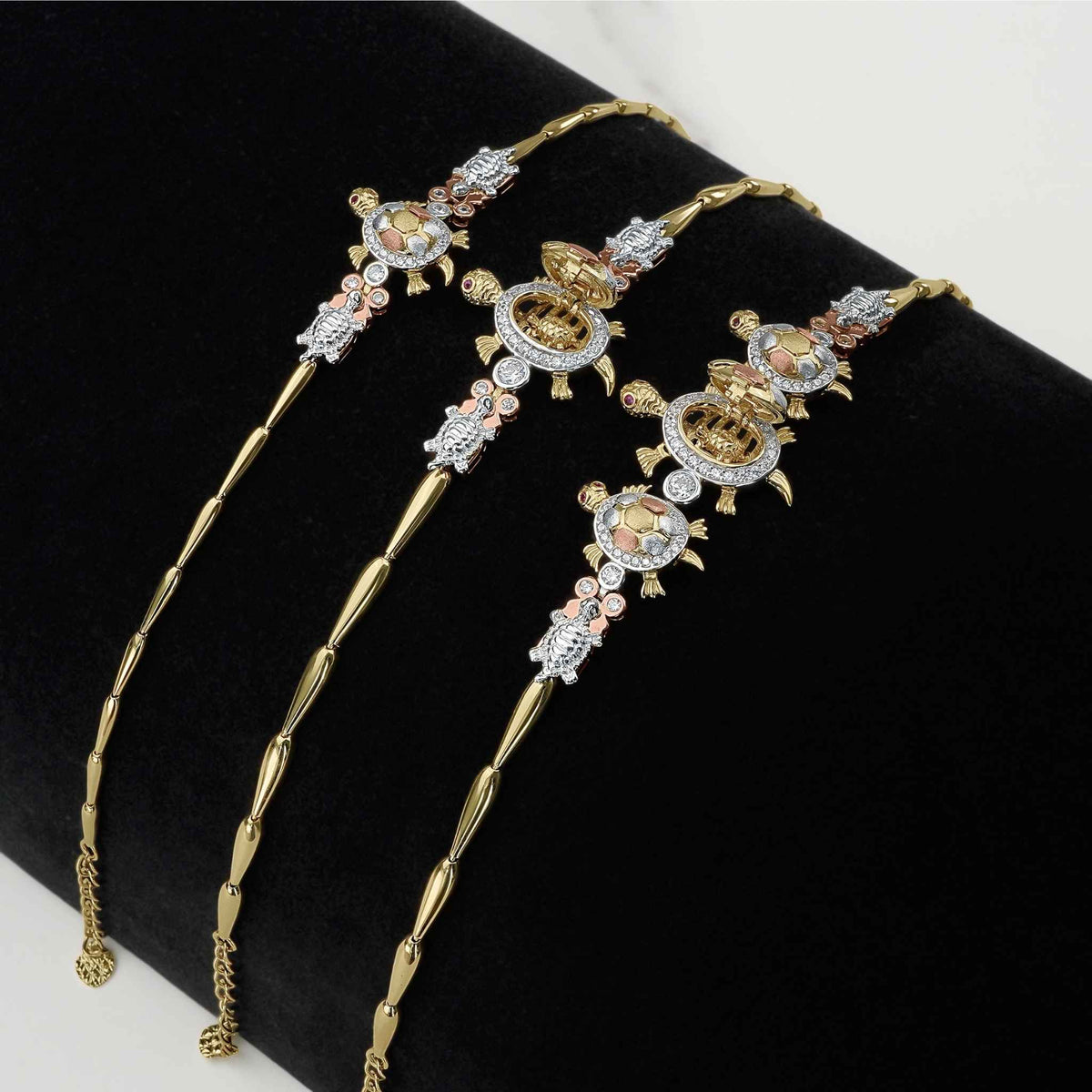Three tricolor gold open-back turtle bracelets displayed on a black velvet stand.