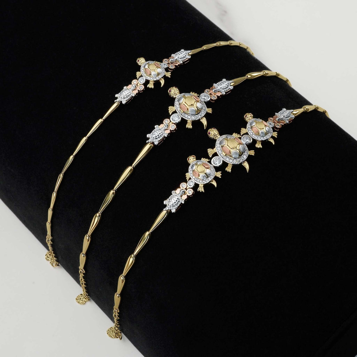 Tricolor gold turtle bracelets adorned with sparkling CZ stones on a black display.