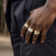 Close-up of a dark-skinned hand wearing three different yellow gold rings with black pants.