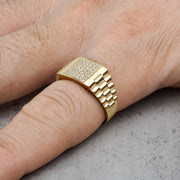 Close-up of a man's finger displaying a gold rectangular ring paved with sparkling stones.