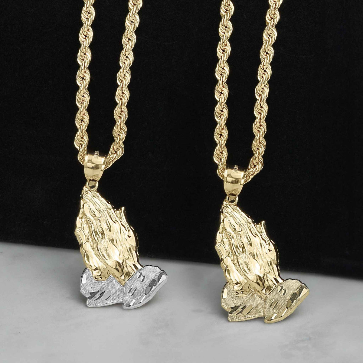 Two gold praying hands pendants, one two-tone and one yellow gold, on chains.