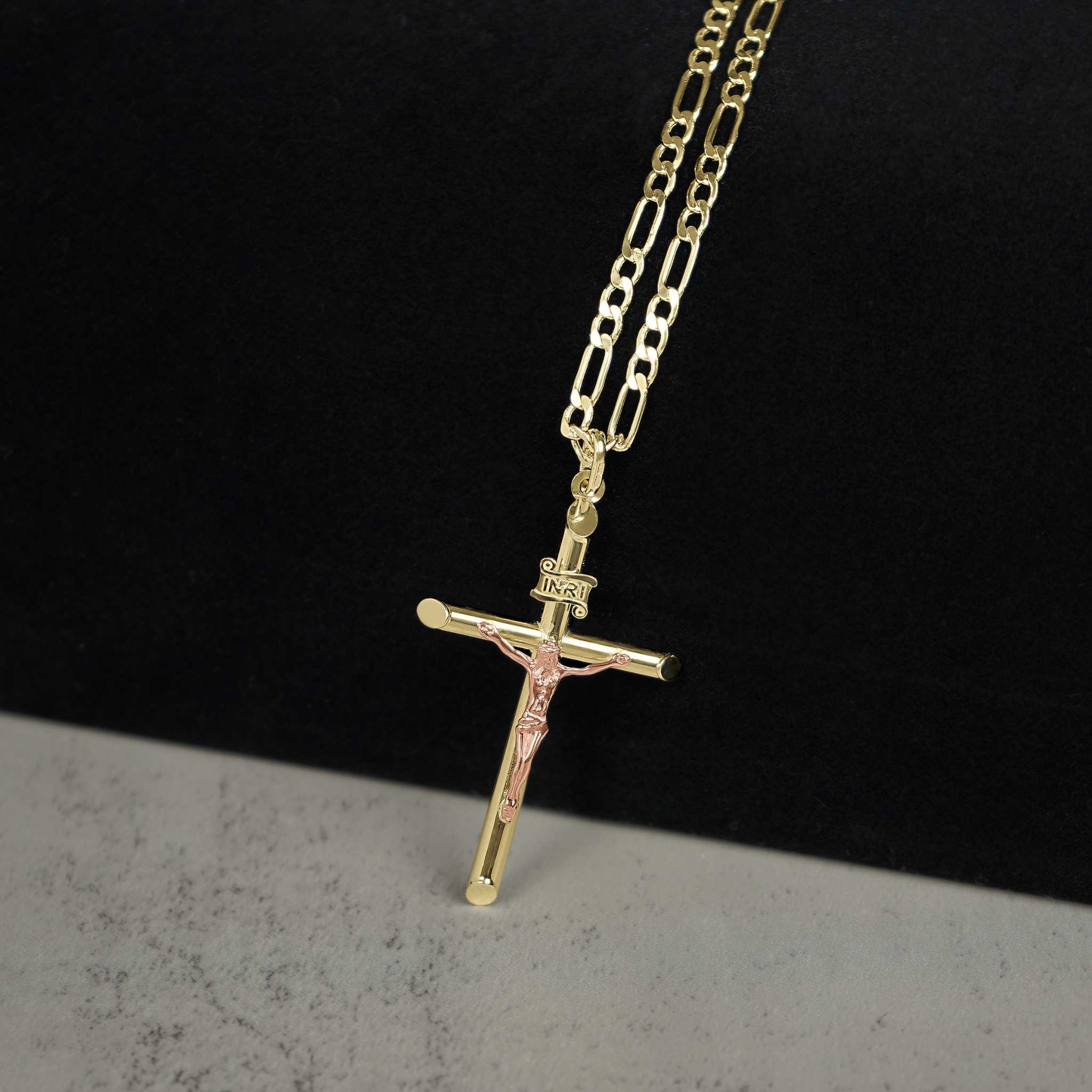 Two-tone gold INRI crucifix pendant hanging on a Figaro chain.