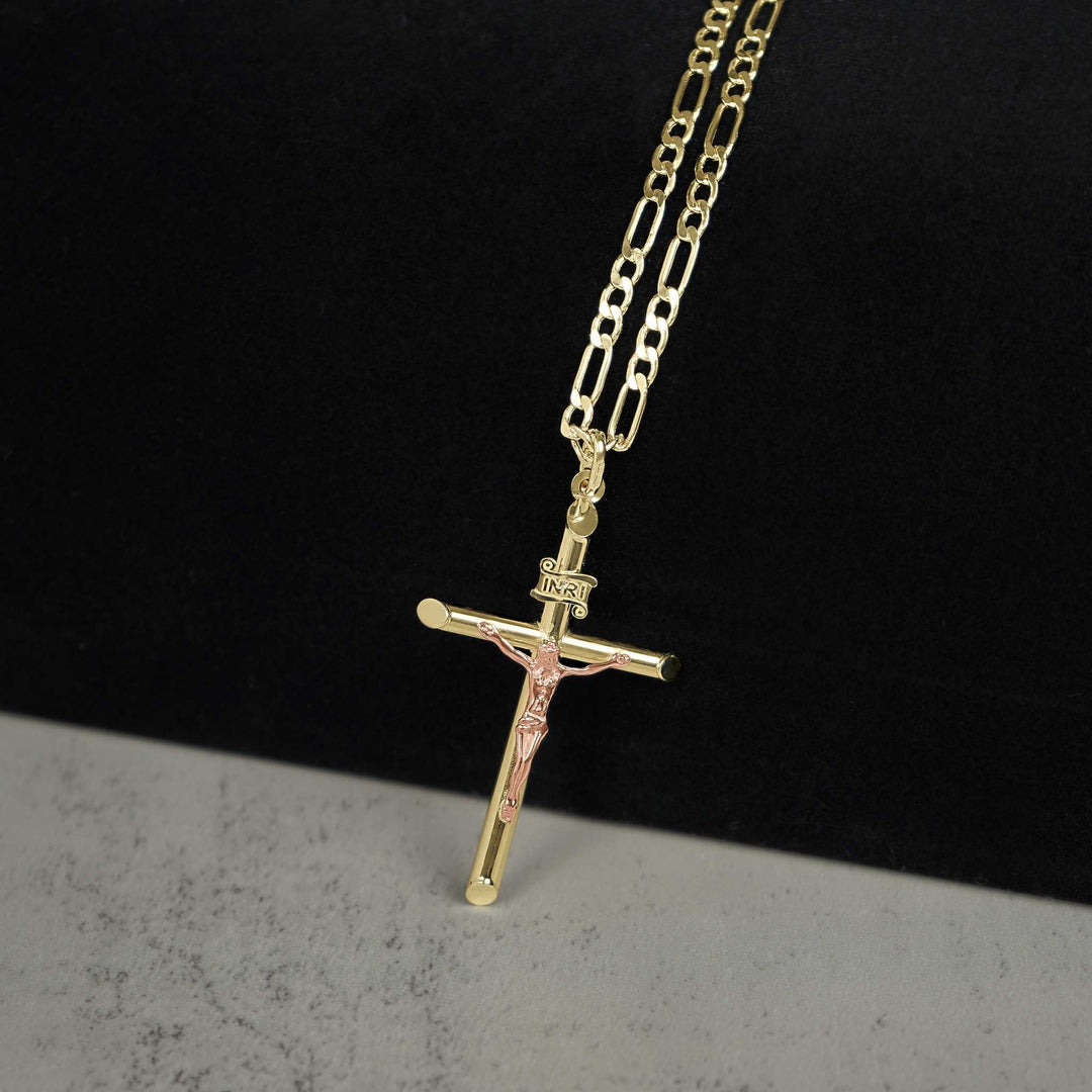 A gold and rose gold crucifix pendant necklace on a paperclip chain against a dark background.