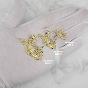 Three yellow gold Saint Michael pendants of varying sizes held in a gloved hand with labels.
