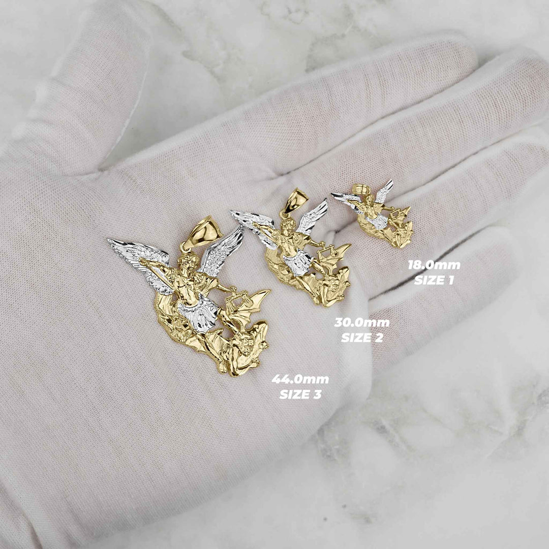 Three gold Saint Michael pendants on a white gloved hand showing different size labels.
