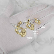 Three gold Saint Michael pendants of varying sizes held in a gloved hand with labels.