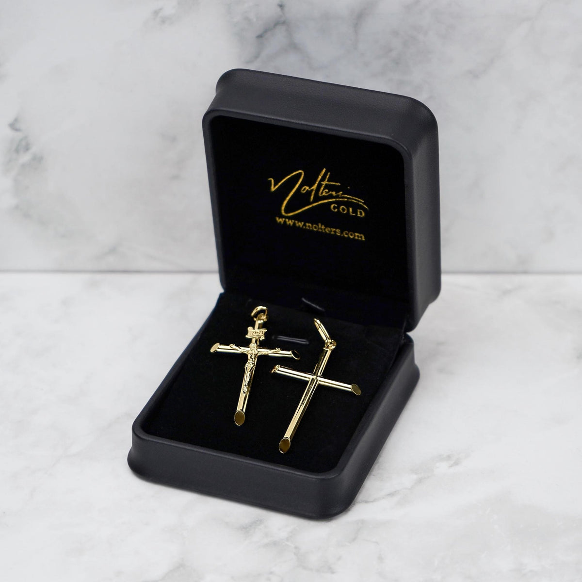 Gold crucifix and tube cross pendants displayed inside an open black jewelry box.