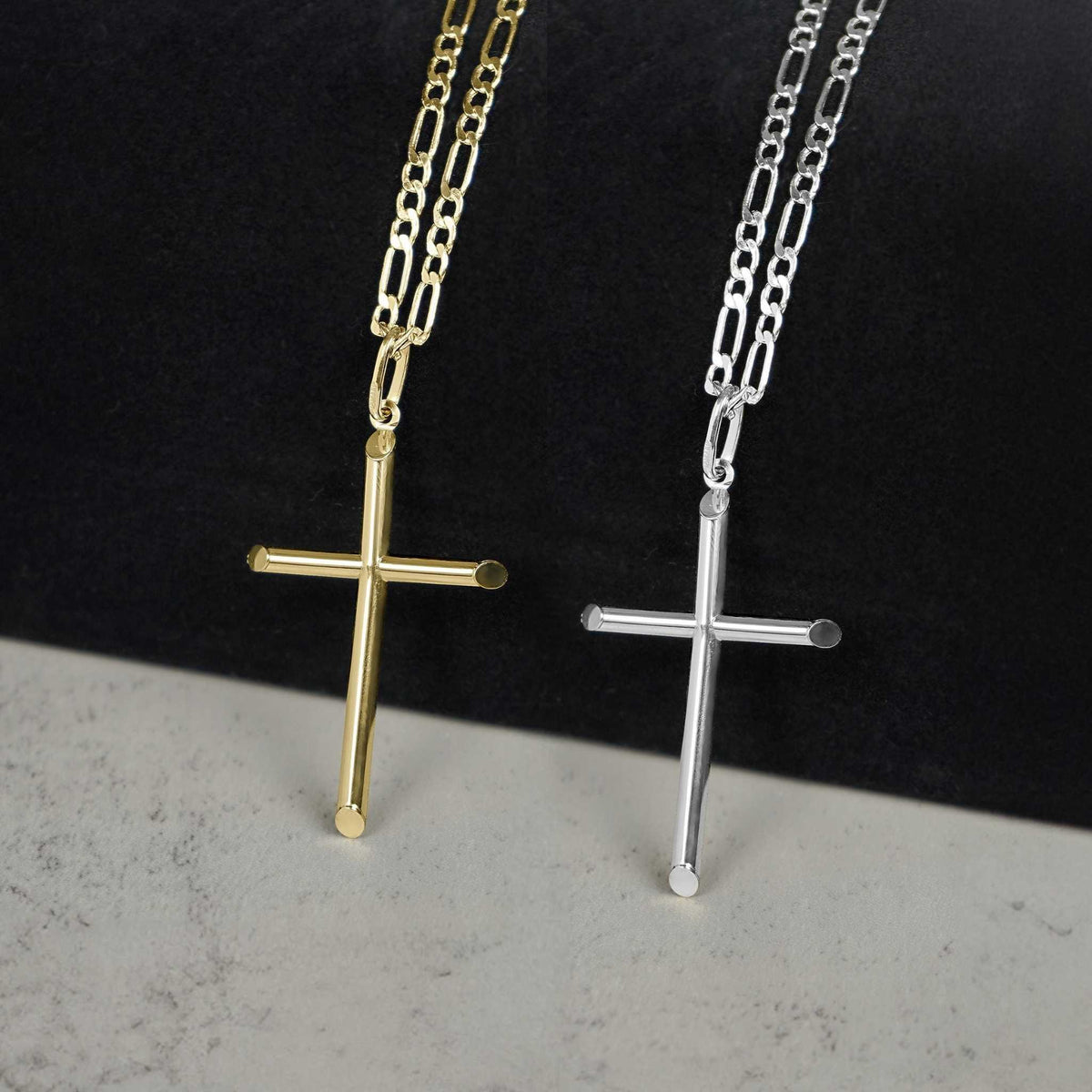 Yellow gold and white gold classic tube cross pendant necklaces on figaro chains displayed side-by-side.