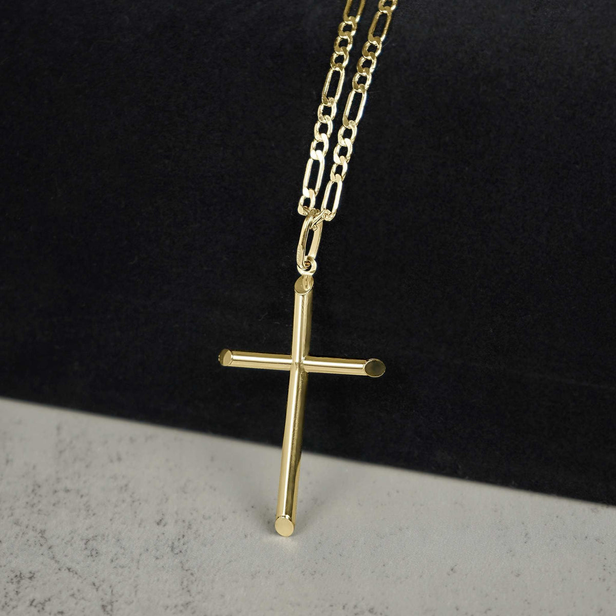 Yellow gold tube cross pendant necklace on a paperclip chain against a two-tone background.