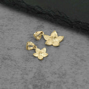 Two gold Fiori hibiscus flower pendant charms displayed on a textured slate surface.