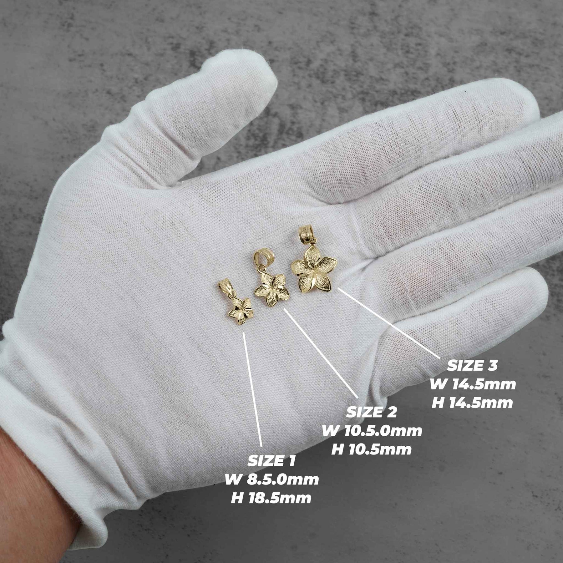 A gloved hand displays three different sizes of gold hibiscus flower pendants with dimension labels.