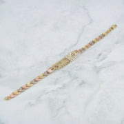 Back view of a tricolor gold quinceañera leaf bracelet resting on white marble.