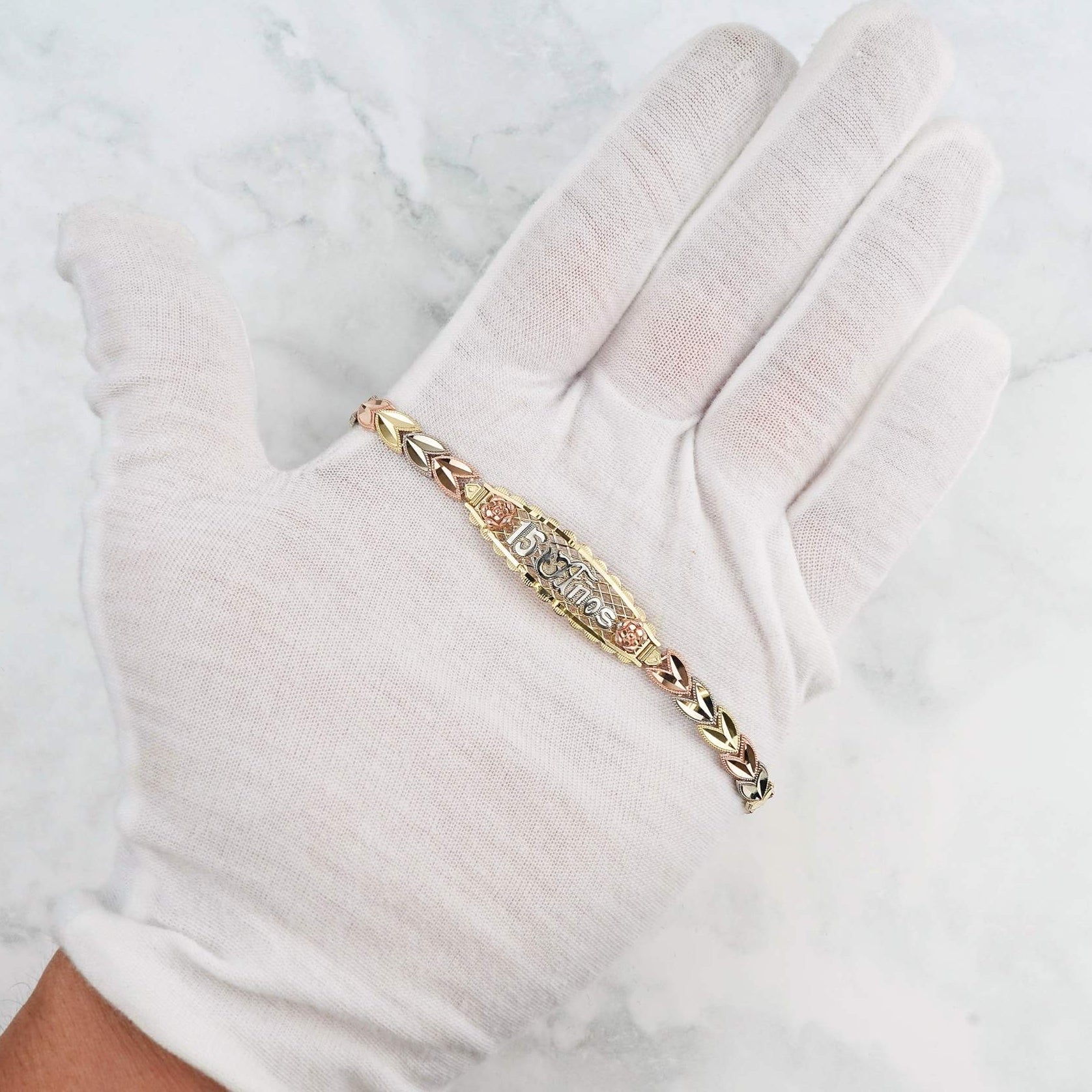 Close-up of the multi-tone gold bracelet with an ornate link design worn on a gloved hand.