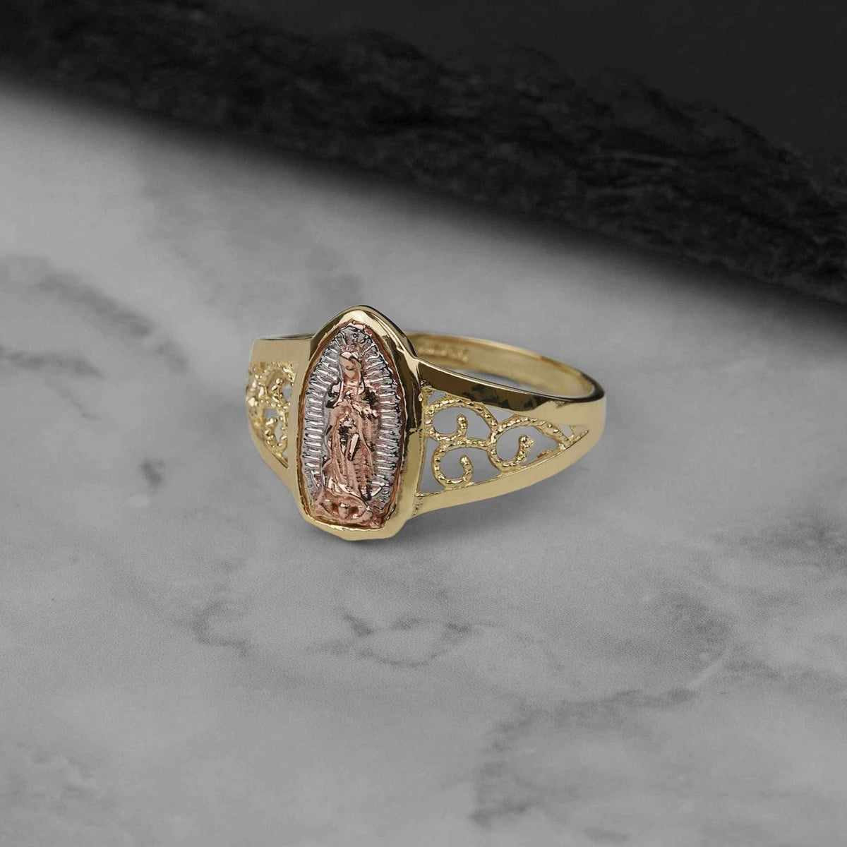 A 10k and 14k gold Alvia pointed oval Virgin Mary ring on a textured surface.