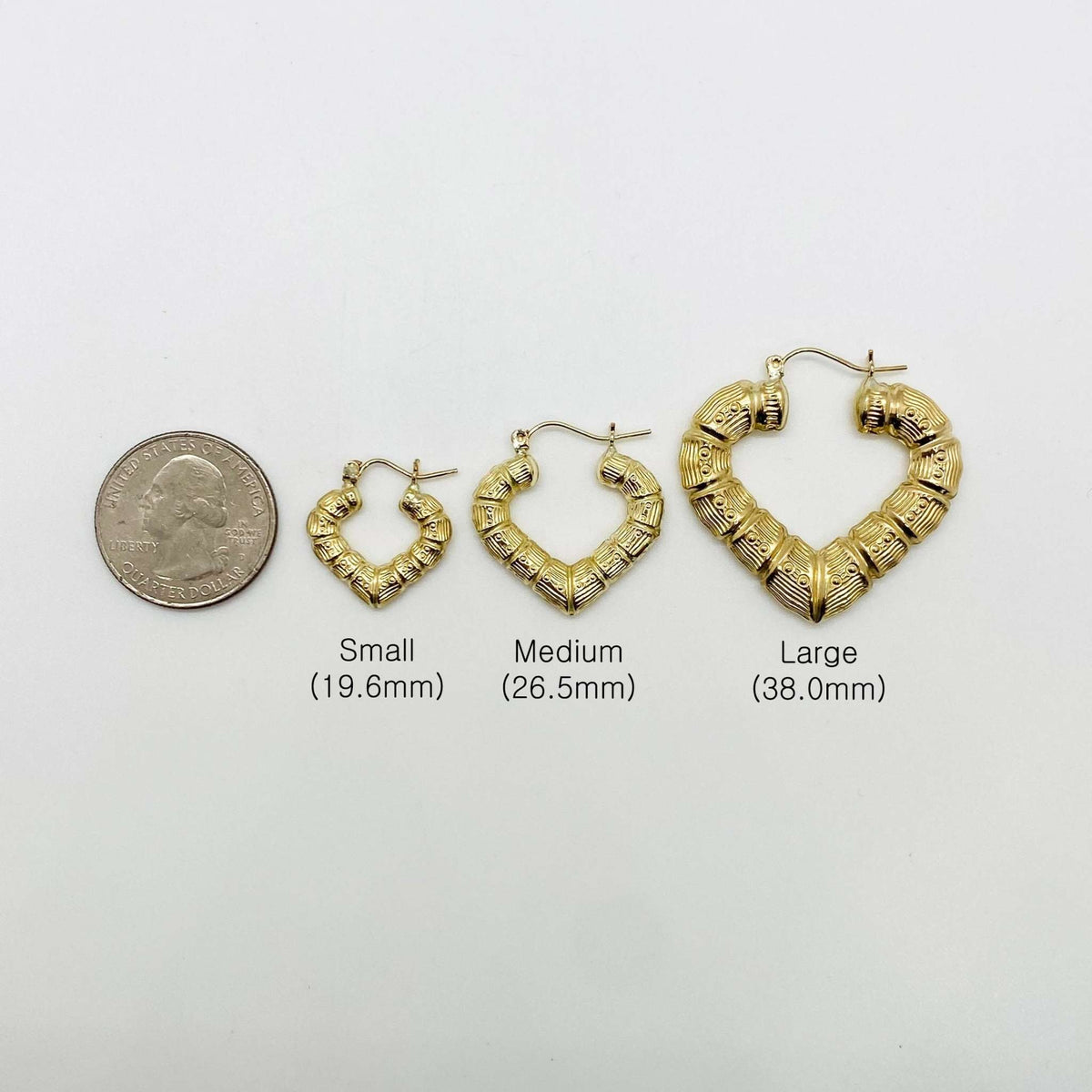 Three sizes of gold bamboo heart hoop earrings arranged next to a quarter.