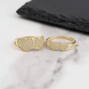 Two gold dual heart rings with pavé white CZ stones on white marble surface