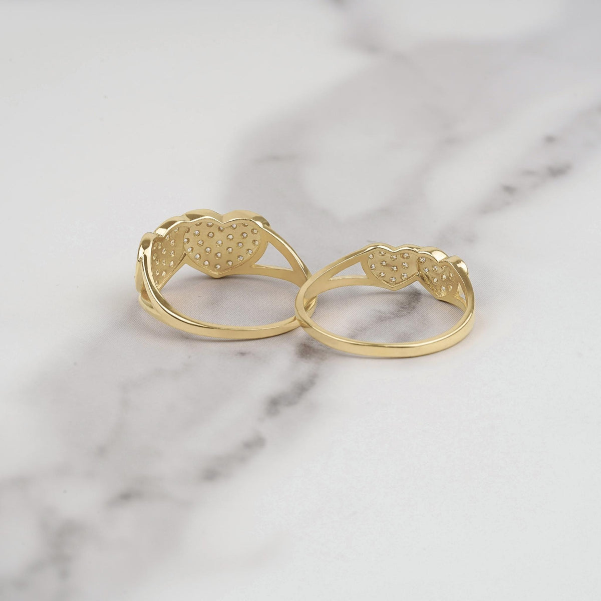 Back view of two gold dual heart rings showing textured finish on white marble surface