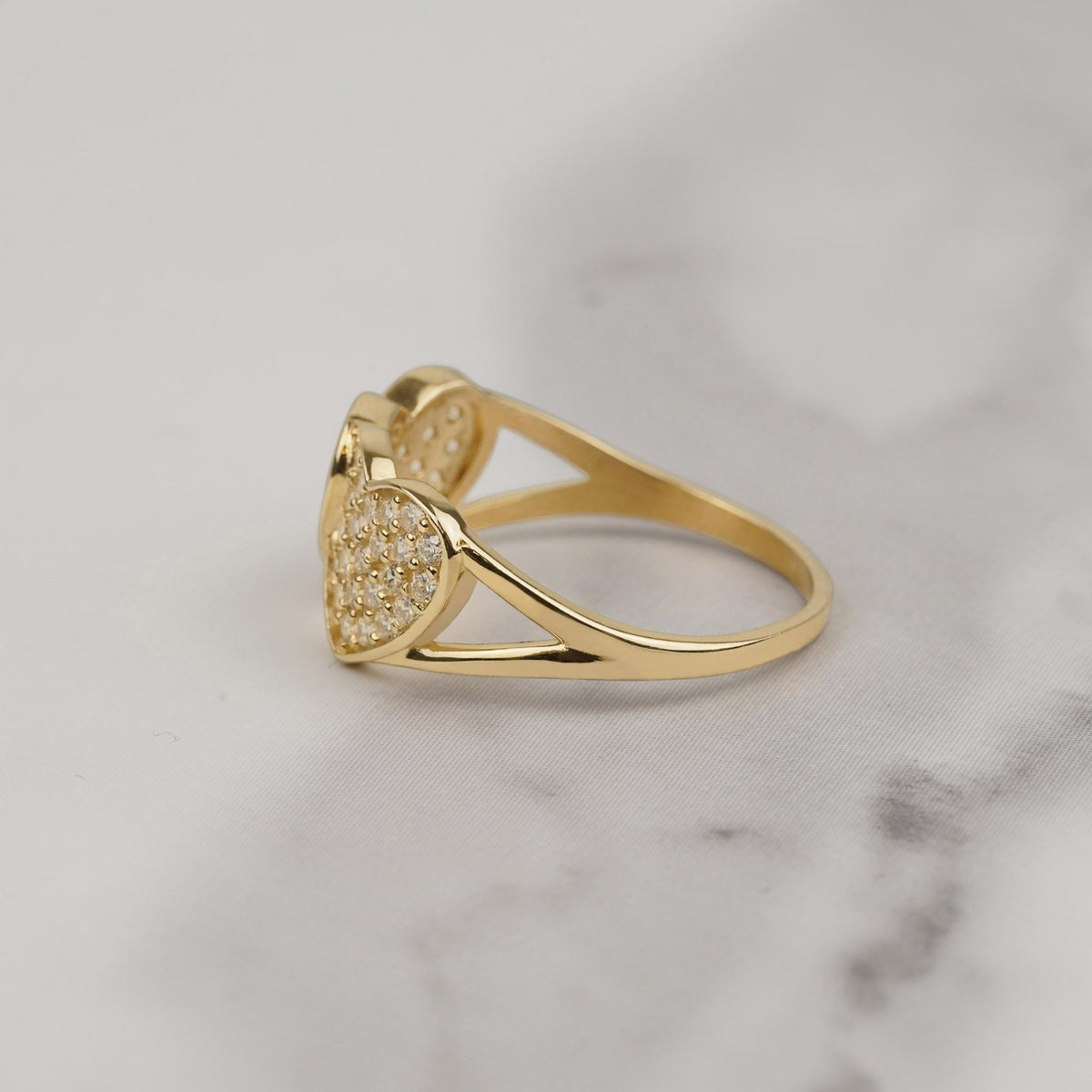 Side profile of a gold dual-heart cubic zirconia ring on white marble.