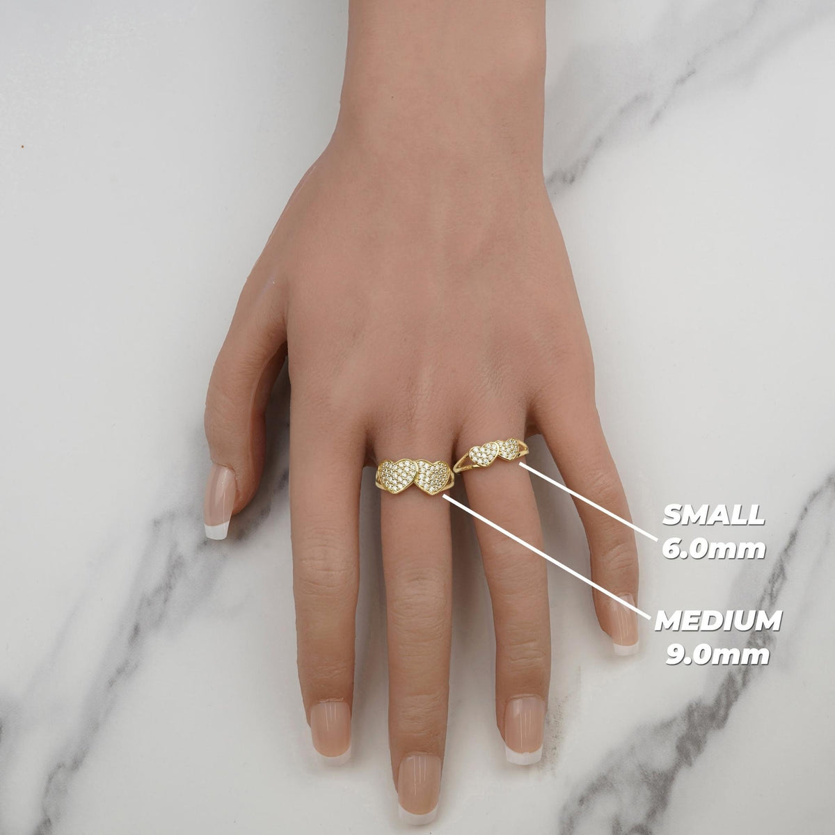 Hand wearing small and medium gold dual-heart rings labeled with heart dimensions.