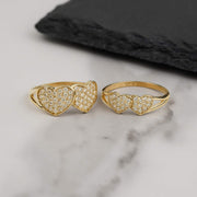 Two gold dual-heart cubic zirconia rings displayed on a white marble background.
