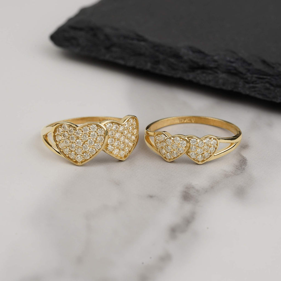 Two gold dual-heart cubic zirconia rings displayed on a white marble background.