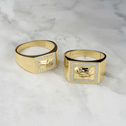 Two gold rectangle nugget rings with cubic zirconia borders on a marble surface.