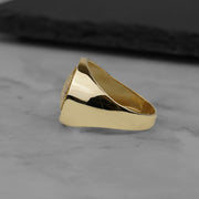 Side profile view of a solid gold round signet ring with a smooth polished band.