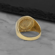 Top-down view of a polished yellow gold round signet ring with a gemstone-paved center.