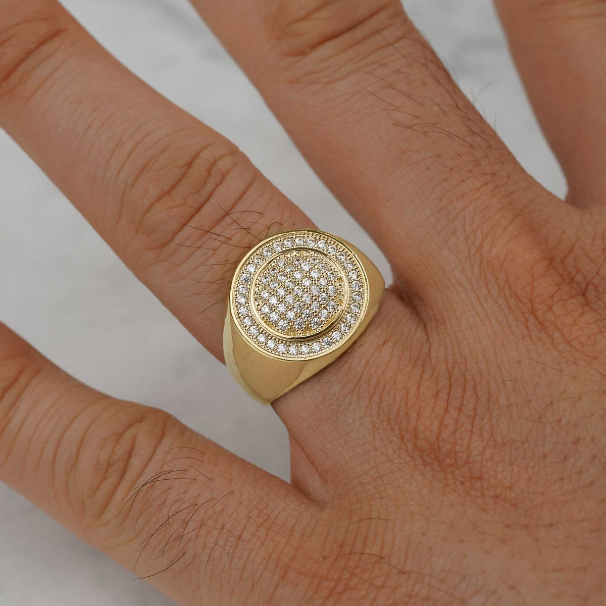 Close-up of a sparkling yellow gold iced-out signet ring worn on a finger.