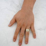 Overhead view of a hand wearing a yellow gold iced-out round signet ring.
