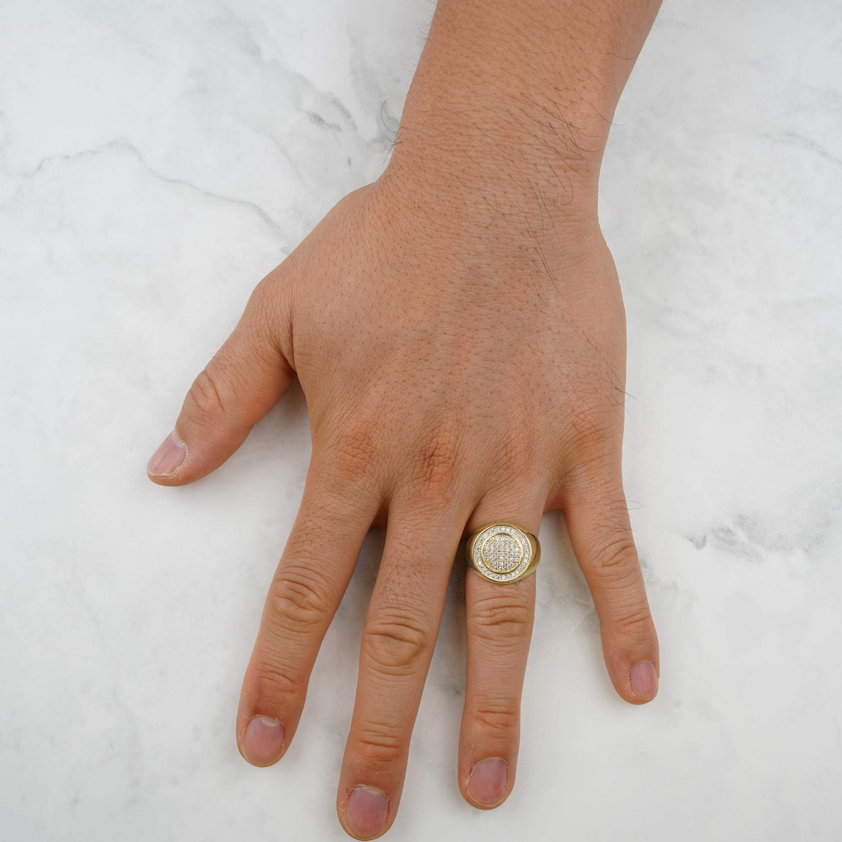 Overhead view of a hand wearing a yellow gold iced-out round signet ring.