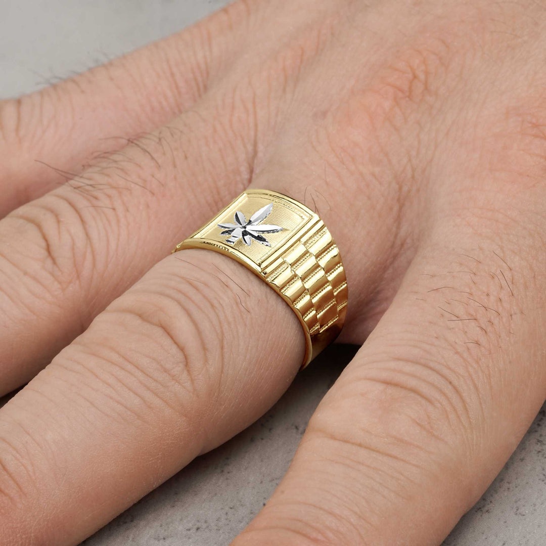 Close-up of a gold Rolex-style ring with a silver cannabis leaf worn on a finger.