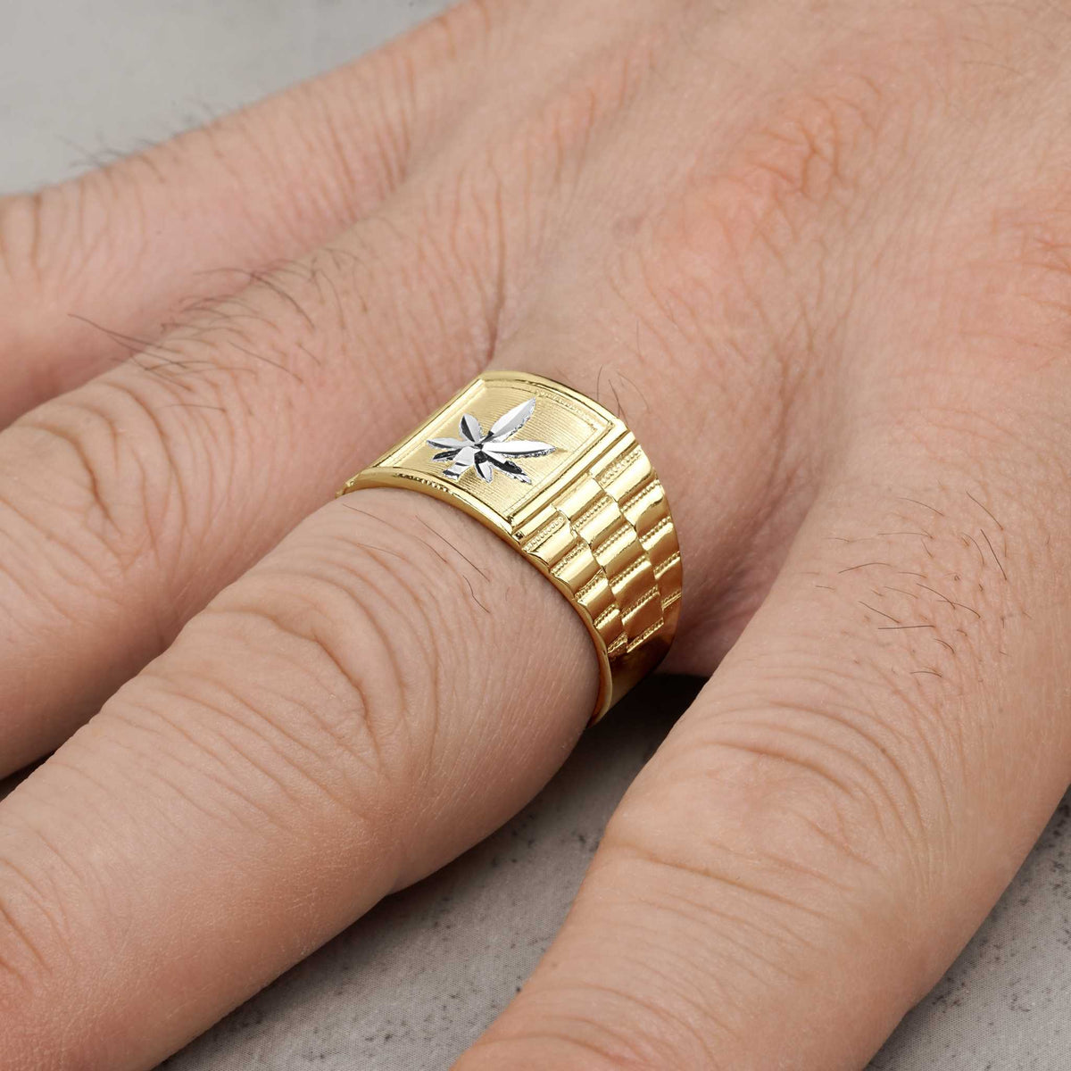 Close-up of a gold Rolex-style ring with a silver cannabis leaf worn on a finger.