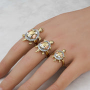 Three tricolor gold Cari turtle rings worn on a hand against a marble background