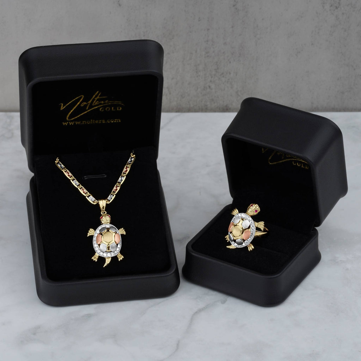 Tricolor gold turtle pendant necklace and matching ring displayed in black jewelry gift boxes.