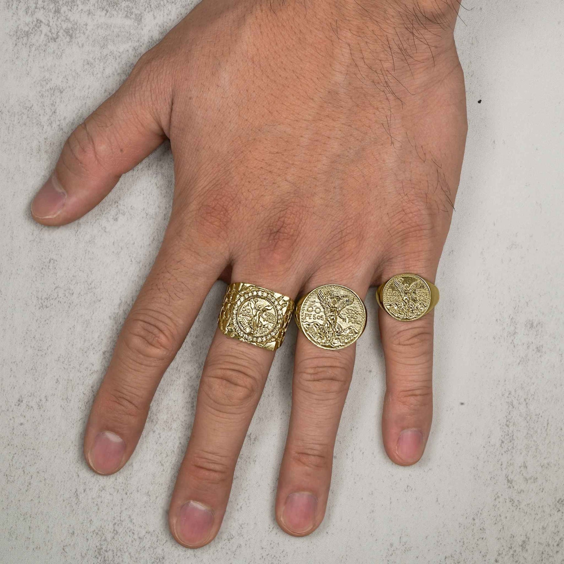 Small, medium, and large gold Centenario square coin rings modeled on a hand.