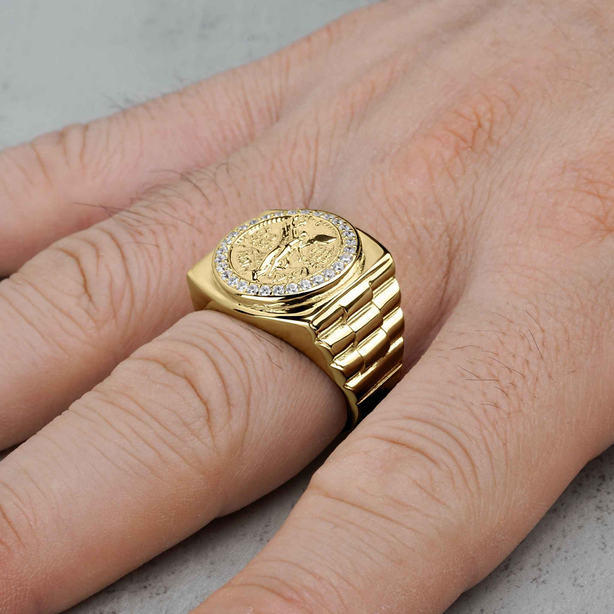 Close-up of men's gold Centenario pesos ring with cubic zirconia border on a hand.