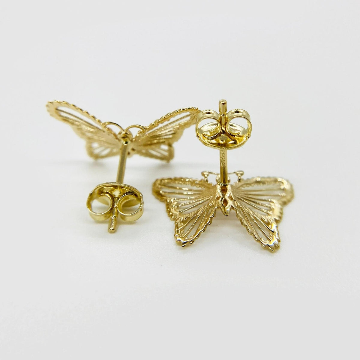 Rear view of gold butterfly stud earrings showing intricate textured cutouts and push-back posts.
