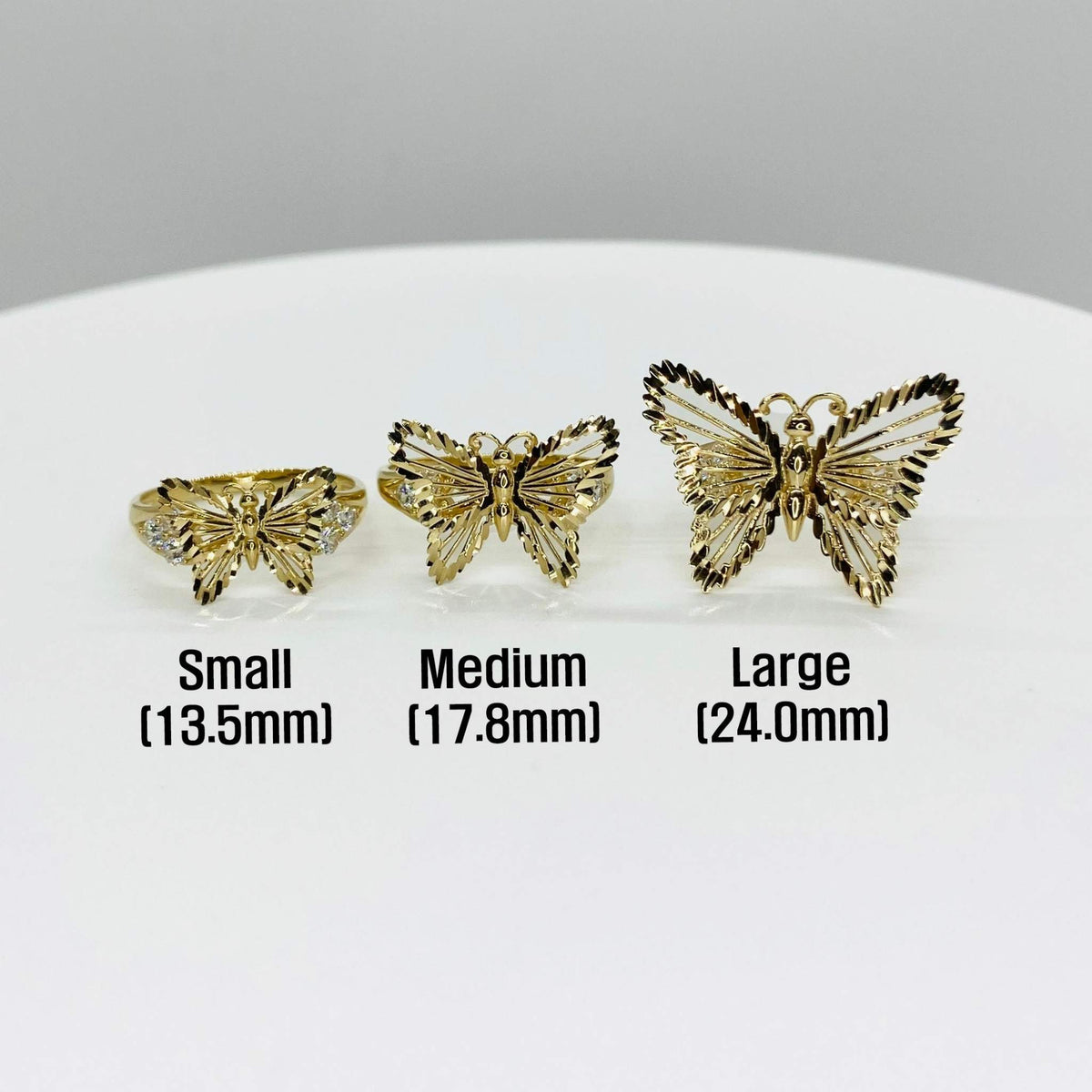 Three 10k - 14k gold butterfly shaped rings in different sizes on a white surface.