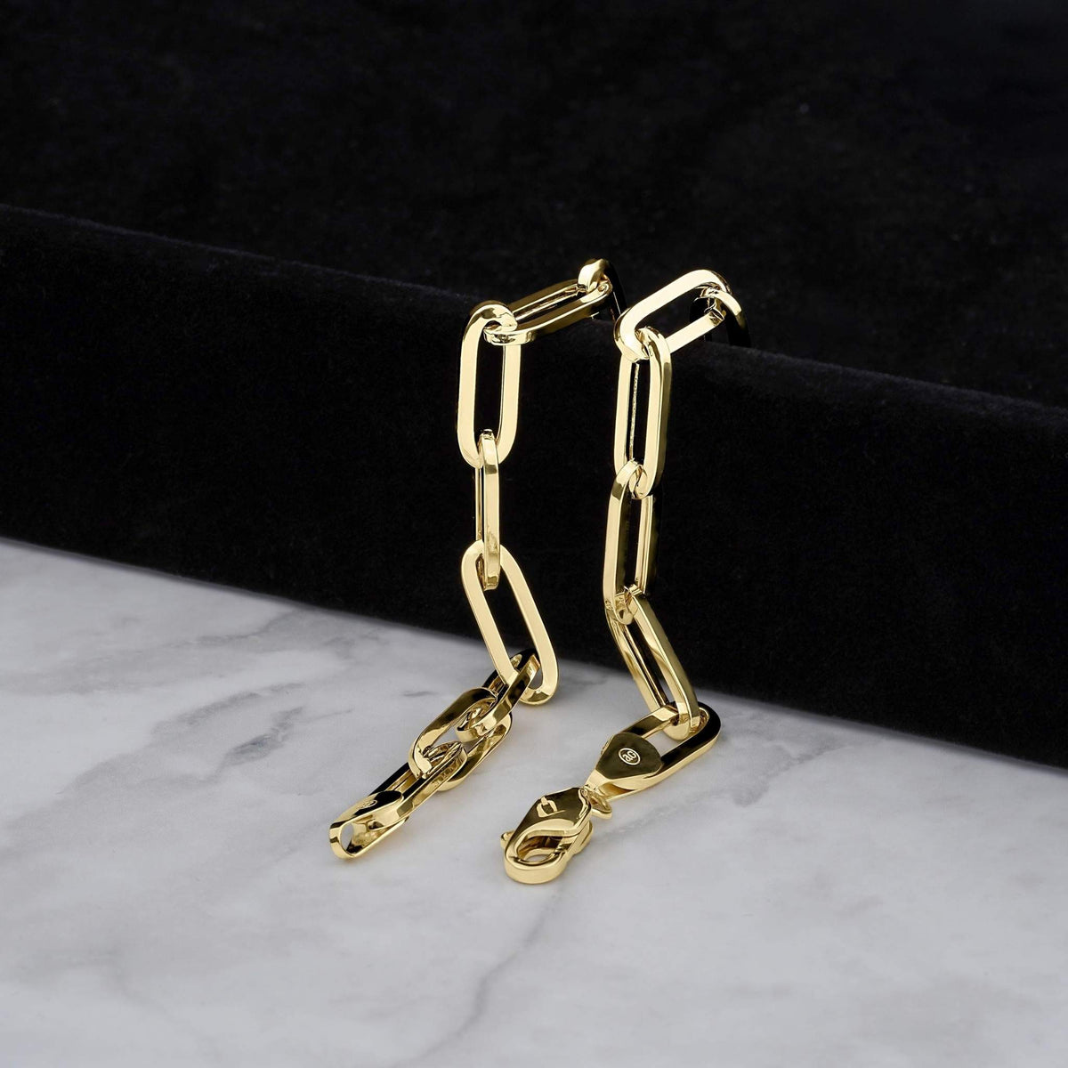 Close-up of two hollow yellow gold paperclip bracelets showing lobster claw clasps.