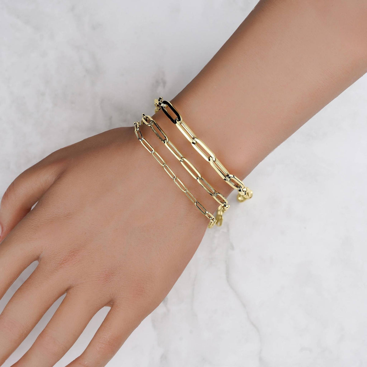 Three hollow yellow gold paperclip chain bracelets stacked on a wrist.